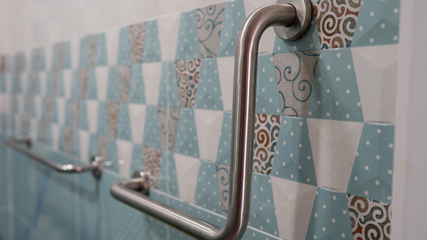 Barra de apoyo de acero inoxidable instalada junto al inodoro en un baño con azulejo decorado