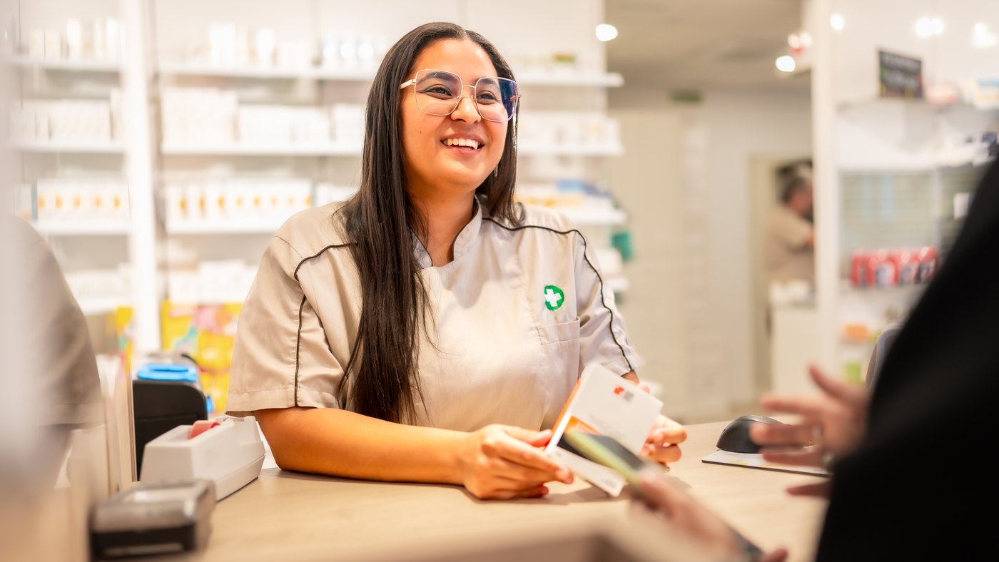 Farmacéutica sonriente atiende a una clienta en el mostrador de una farmacia