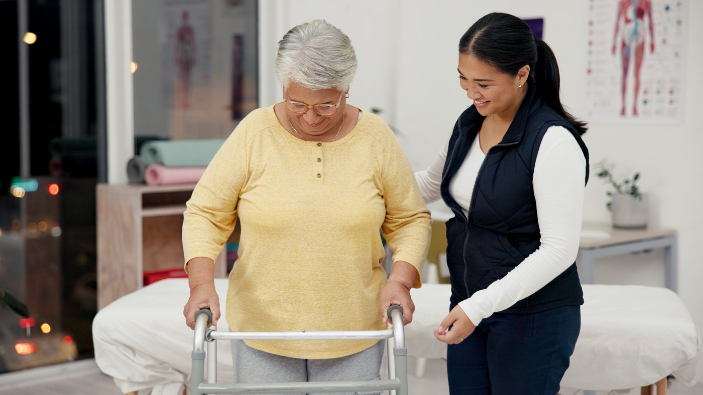 Fisioterapeuta orienta a una adulta mayor mientras prueba una andadera en consultorio