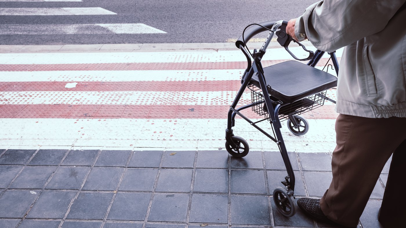 Adulto mayor con andadera con ruedas y asiento esperando para cruzar la calle